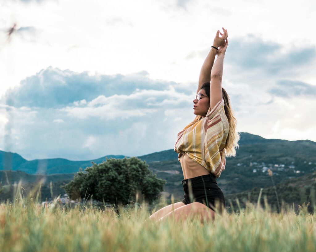 Woman practicing yoga pose in a scenic outdoor field with mountains.
